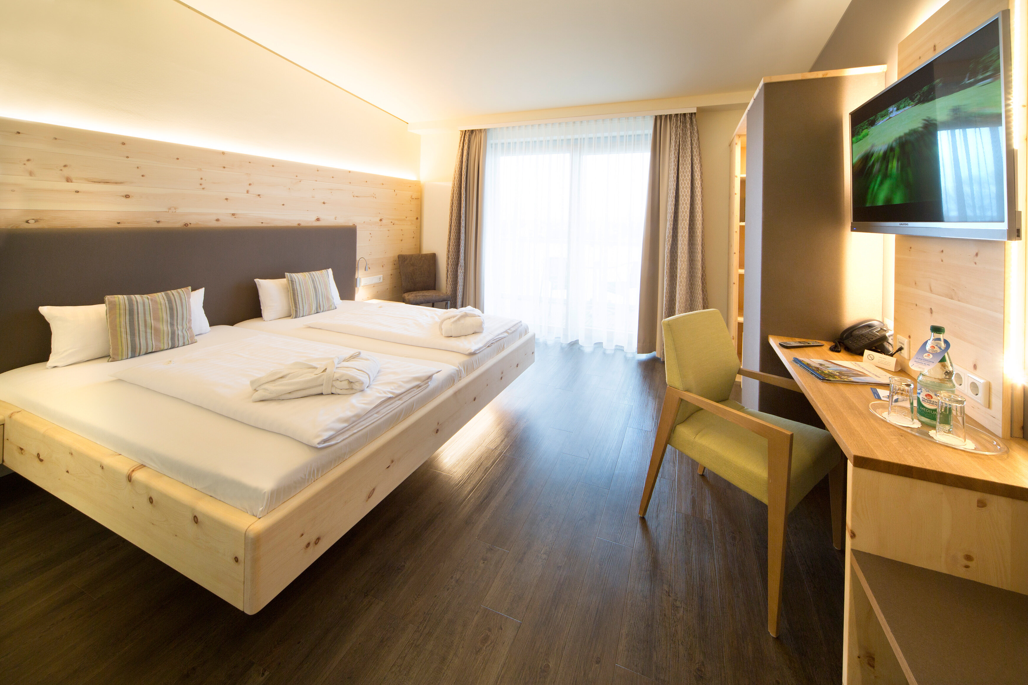 Das Bild zeigt einen Blick in das Doppelzimmer Zirbe mit Zirbenbett, Schreibtisch, vertäfelter Wand aus Zirbenholz und Fenster zum Balkon 