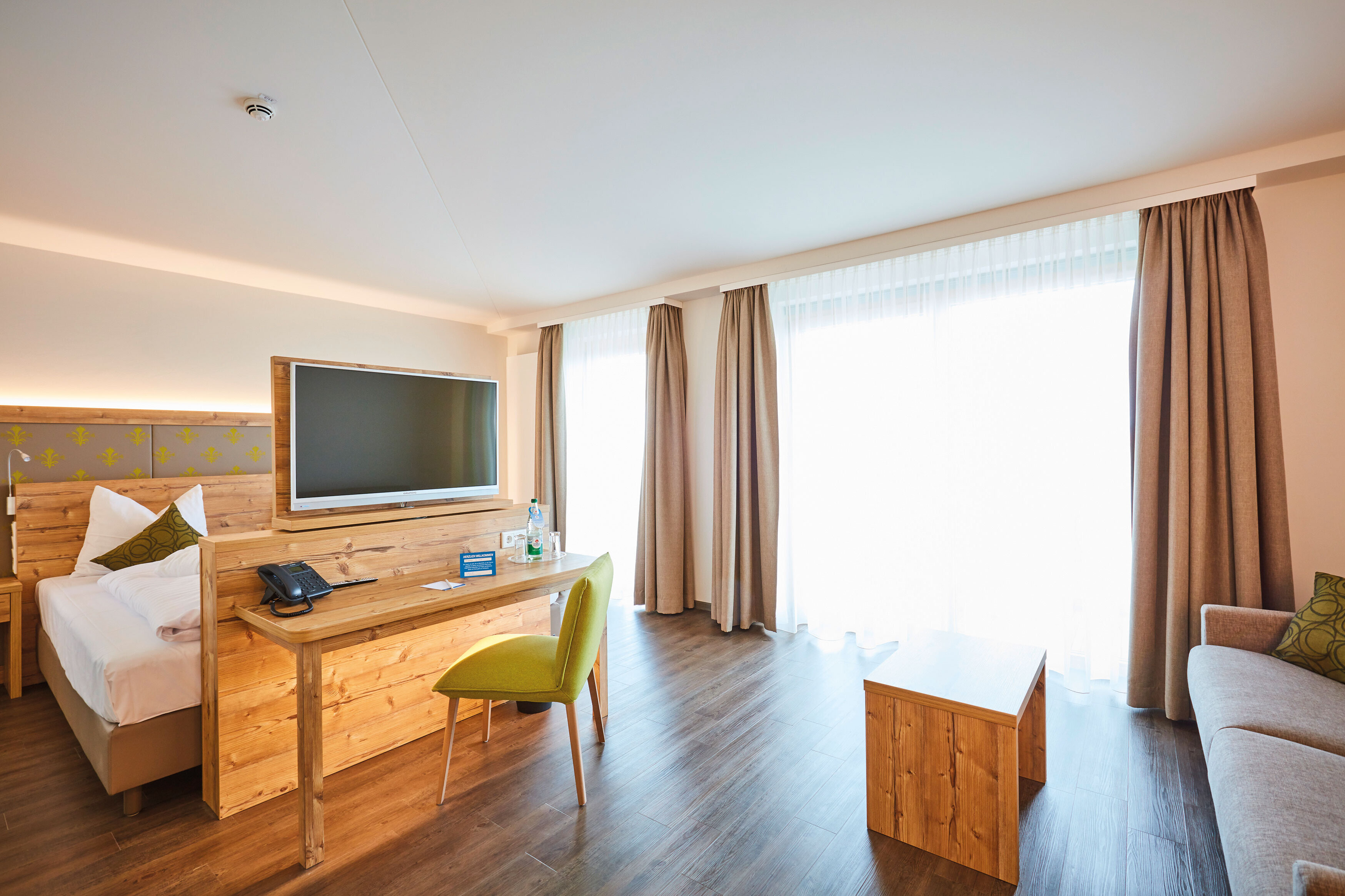 Das Bild zeigt einen Blick in das Doppelzimmer Superior mit Bett, Schreibtisch mit drehbarem Fernseh-Panel, Couch und Couchtisch